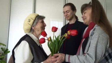 Olgun Kız ve Genç Yetişkin Torun Yaşlı Anne 'ye Hediyeyi ve Lale Çiçeklerini Ziyaret Edin. Mutlu kıdemli kadın ailesinin onu ziyaret ettiğini gördüğüne sevindi. 2x Yavaş çekim 0.5 hız 60 fps 4K