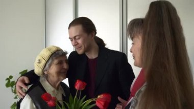 Olgun Kız ve Genç Yetişkin Torun Yaşlı Anne 'ye Hediyeyi ve Lale Çiçeklerini Ziyaret Edin. Mutlu kıdemli kadın ailesinin onu ziyaret ettiğini gördüğüne sevindi. 2x Yavaş çekim 0.5 hız 60 fps 4K