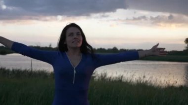 Mutlu Kadın Gün Batımında Yağmurda Dönen Dans Ediyor. Özgürlük Duyguları 'nın tadını çıkarıyorum. Nehir kenarındaki manzara ve fırtınalı hava durumu dramatik bulutlar. 2x Ağır çekim 1 / 2 60 fps