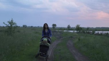 Genç Anne Bebek Arabası İterek Sunset 'te Düşünüyor ve Bakıyor. Manzaralı Doğa Gecesi Alacakaranlığı, Alacakaranlık. Fırtınalı Yağmurlu Hava Dramatik Bulutlar Gökyüzü. 2x Ağır çekim - 1 / 2 60 fps