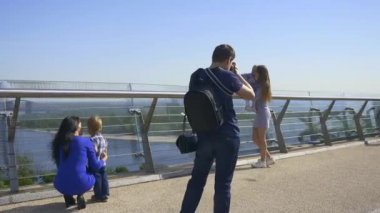 Fotoğrafçı, Çocuklarla Annelerin Fotoğraflarını Çekiyor. Şehir Arkaplanı 'ndaki Pedestrian Köprüsü' nde Sahne Arkası Fotoğraf Oturumu