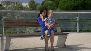 Anne, çocuğuyla birlikte şehir parkındaki Bench 'te oturuyor. Şehir Yeşil Alanı. Parlak Güneşli Yaz Günü
