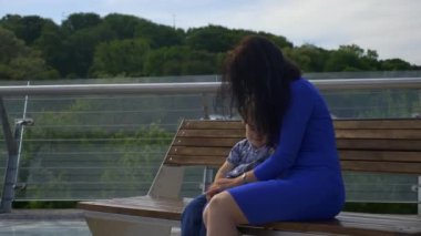Anne, çocuğuyla birlikte şehir parkındaki Bench 'te oturuyor. Şehir Yeşil Alanı. Parlak Güneşli Yaz Günü