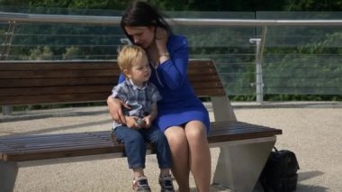 Anne, çocuğuyla birlikte şehir parkındaki Bench 'te oturuyor. Şehir Yeşil Alanı. Parlak Güneşli Yaz Günü