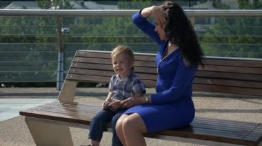 Anne, çocuğuyla birlikte şehir parkındaki Bench 'te oturuyor. Şehir Yeşil Alanı. Parlak Güneşli Yaz Günü