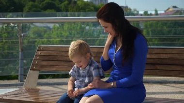 Anne, çocuğuyla birlikte şehir parkındaki Bench 'te oturuyor. Şehir Yeşil Alanı. Parlak Güneşli Yaz Günü