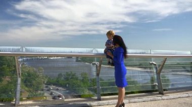 Anneyi Sevmek, Çocuğu Sarmak, Ellerini Köprü 'de Tutmak. Şehir Arkaplanı Mavi Gökyüzü Parlak Güneşli Günü. 2x Ağır çekim 1 / 2 60 FPS