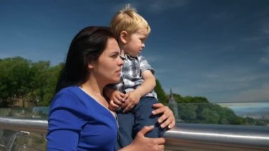 Anne, Oğul 'a Çevre' den bahseder - Elleri Köprüde Tutarken Uzakta Parmağını Uzakta Tutan Çocuğu Gösterir. Şehir Arkaplanı Mavi Gökyüzü Parlak Güneşli Günü. 2x Ağır çekim 1 / 2 60 FPS