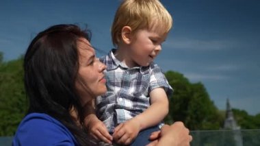 Anneyi Sevmek, Çocuğu Sarmak, Ellerini Köprü 'de Tutmak. Şehir Arkaplanı Mavi Gökyüzü Parlak Güneşli Günü. 2x Ağır çekim 1 / 2 60 FPS