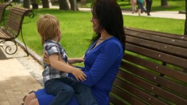 Anne, çocuğuyla birlikte şehir parkındaki Bench 'te oturuyor. Şehir Yeşil Alanı. Parlak Güneşli Yaz Günü