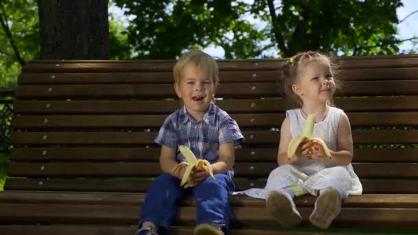 Happy Boy Girl Siedzą Ławce Parku Dzieci Jedzą Banany Jasny — Wideo stockowe