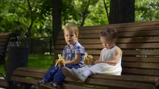 Happy Boy Girl Siedzą Ławce Parku Dzieci Jedzą Banany Jasny — Wideo stockowe