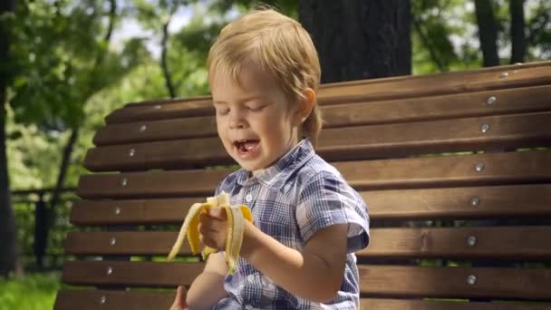 Radosny Chłopiec Śpiewa Piosenkę Jedząc Banana Dziecko Siedzi Ławce Parku — Wideo stockowe