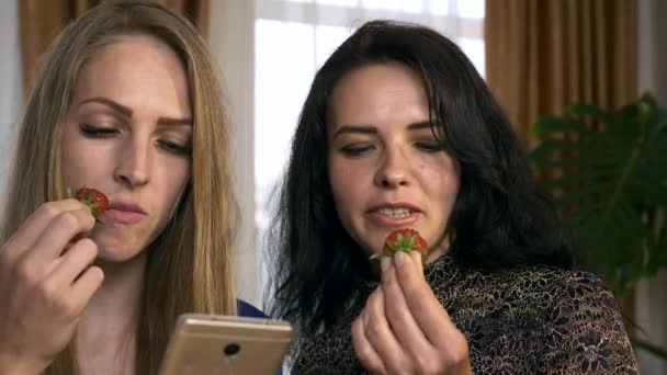 2人の女性の友人は自宅でスマートフォンでソーシャルメディアを共有し 見てチャットしながらイチゴを食べる 2倍スローモーション 5速度60 Fps — ストック動画