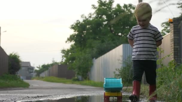 Kleiner Junge Spaziert Und Spielt Nach Dem Regen Mit Spielzeugwagen — Stockvideo