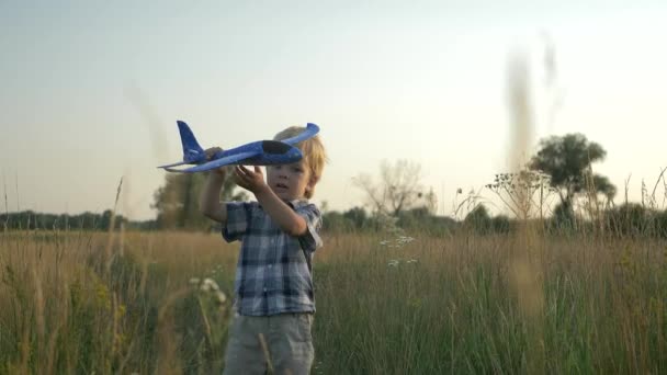 Petit garçon jouant et courant avec l'avion de jouet à travers le champ d'herbe élevé. Paysage rural du coucher du soleil. 2x Mouvement lent - Demi-vitesse 60 FPS 
