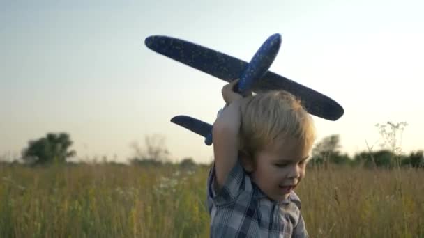 芝生広場の向こうでおもちゃの飛行機で遊んで走っている小さな男の子 田舎の夕日の風景 2倍スローモーション ハーフスピード60 Fps — ストック動画