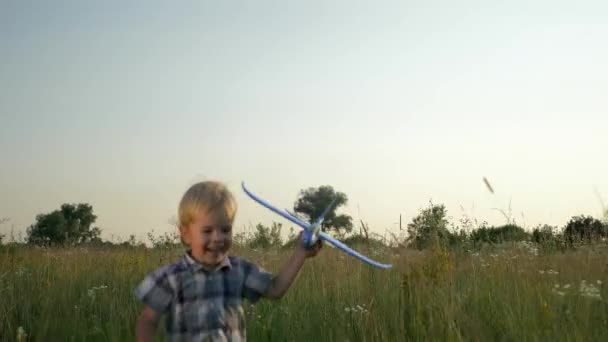 芝生広場の向こうでおもちゃの飛行機で遊んで走っている小さな男の子 田舎の夕日の風景 2倍スローモーション ハーフスピード60 Fps — ストック動画