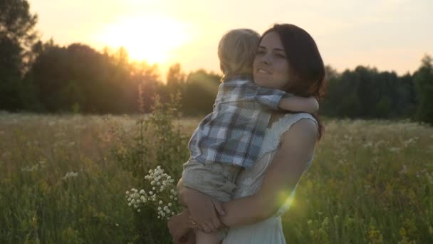 Šťastný milující matka objímání roztomilý malý syn. Rodina odpočívající na krásné přírodě. Sunset Sun Beams Flares. Večerní venkovská scéna. 2x Zpomalení - Poloviční rychlost 60 FPS