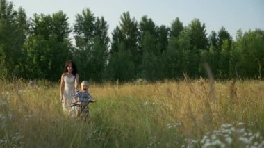 Küçük Çocuk Kırsal Yol 'da Dolaşan Genç Anne' ye yardım ederek Çocuk Bisikleti Sürmeyi Öğreniyor. Yaz Akşamı. 2x Slow motion - Yarı hız 60 FPS