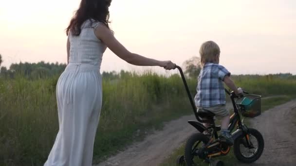 Little Boy Aprende Andar Bicicleta Infantil Com Ajuda Jovem Mãe — Vídeo de Stock