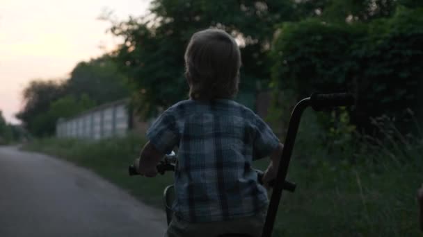 小さな男の子は田舎道を散歩する若い母親を助けることで子供の自転車に乗ることを学びます 夏の夜 2倍スローモーション ハーフスピード60 Fps — ストック動画
