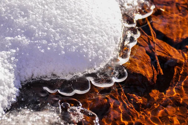 渦巻き氷とオレンジの石の下の小川で解凍パッチで水周りの雪 — ストック写真