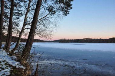 Donmuş göl kıyısında sakin bir akşam. Gökyüzündeşafak ışığı. Erken ilkbahar doğa manzara