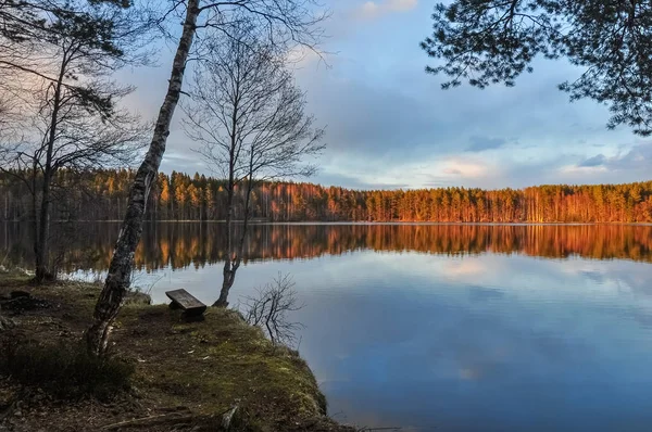 Klidné prostředí. Západ slunce na jezeře. Dřevěná lavička na břehu — Stock fotografie