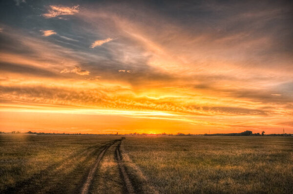 Road in the steppe under amazing cloudy sunset sky.