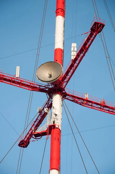 Antenas e antenas parabólicas na torre de telecomunicações vermelho-branca contra o céu azul — Fotografia de Stock