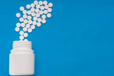 Beyaz tabletler mavi arka plandaki bir şişeden dağılıyor.