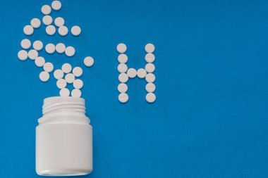 Beyaz tabletler mavi arka plandaki bir şişeden dağılıyor.