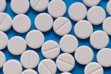 Mavi arka planda beyaz yuvarlak tabletler. Mavi arkaplandaki beyaz kapsüllerin makrosu.