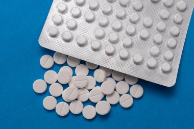 Kabarcık ve beyaz tabletler mavi arka plana saçılmış.