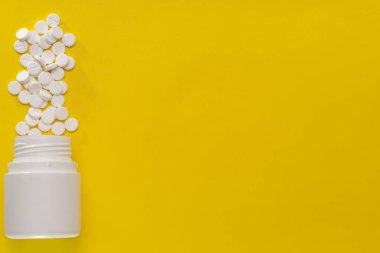 Beyaz tabletler sarı arka planda bir şişeden yayılmış.