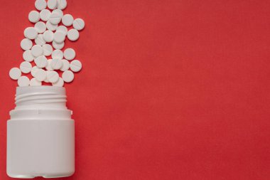 Kırmızı arka plandaki şişeden yayılmış beyaz tabletler.