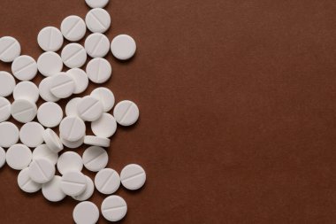 Beyaz tabletler kahverengi arka plandaki bir şişeden dağılmış..