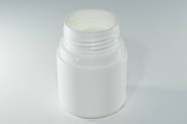 Beyaz arka planda haplar olan beyaz bir şişe.