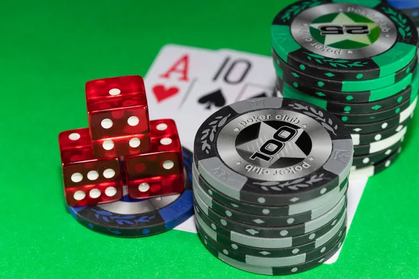 3 red casino dice and chips of different denominations on a green background backdrop. In the background blackjack