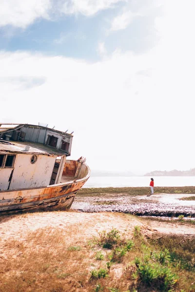 Chica de pie junto al barco abadonado en la orilla — Foto de Stock