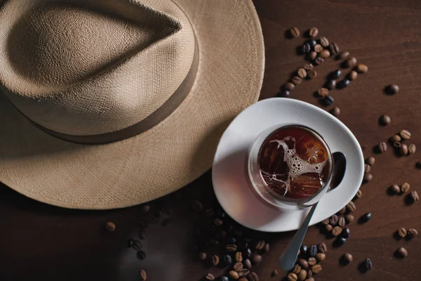 Glas Heißgetränk in Komposition mit Hut und Kaffeekörnern auf Holztisch — Stockfoto