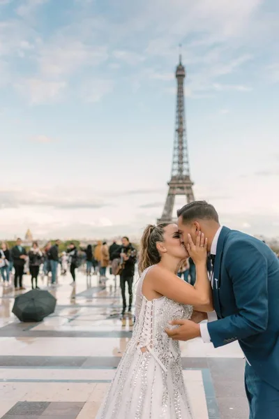 パリを背景にエッフェル塔と情熱的にキスを白いウェディングドレスで青いスーツの膝と花嫁の新郎 — ストック写真
