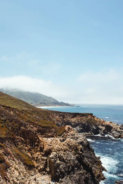 Blauwe golven wassen rotsachtige kust in heldere dag — Stockfoto