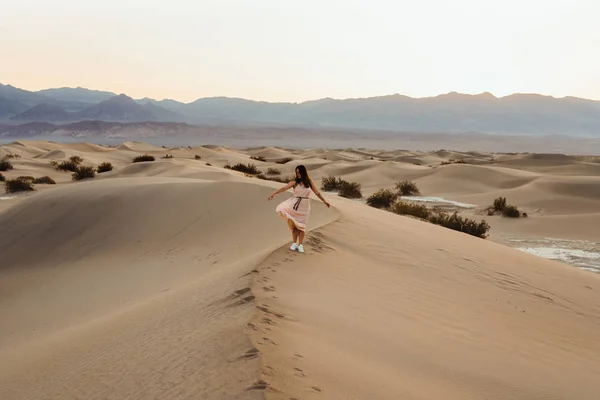 Обратный вид на молодую женщину, идущую по пустыне, оставляющую следы в — стоковое фото