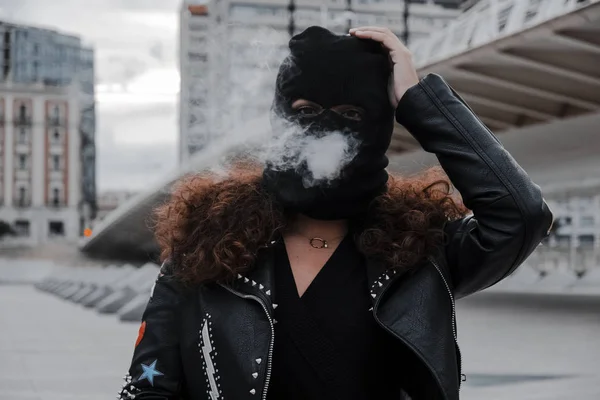 Mulher de máscara preta e jaqueta fumando na rua — Fotografia de Stock