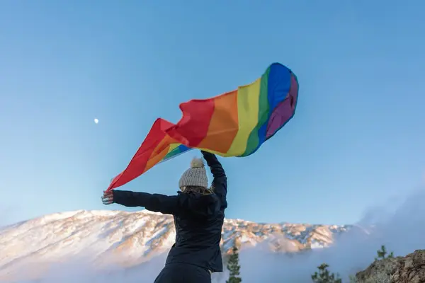 Person on mountain peak waving LGBT flag — Stock Photo, Image