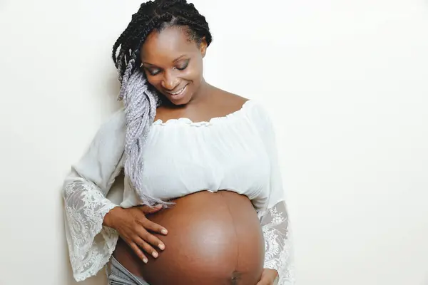 Szczęśliwa Afroamerykanka w ciąży trzyma się za ręce na brzuchu — Zdjęcie stockowe