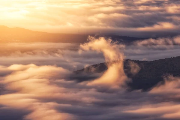 日の出の柔らかい白い厚い雲の間で強力な山々の黒いピークの上から — ストック写真