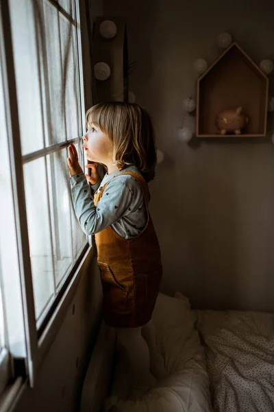 Urocza Dziewczynka Ubraniu Casual Patrząc Przez Okno Podczas Odpoczynku Przytulnym — Zdjęcie stockowe